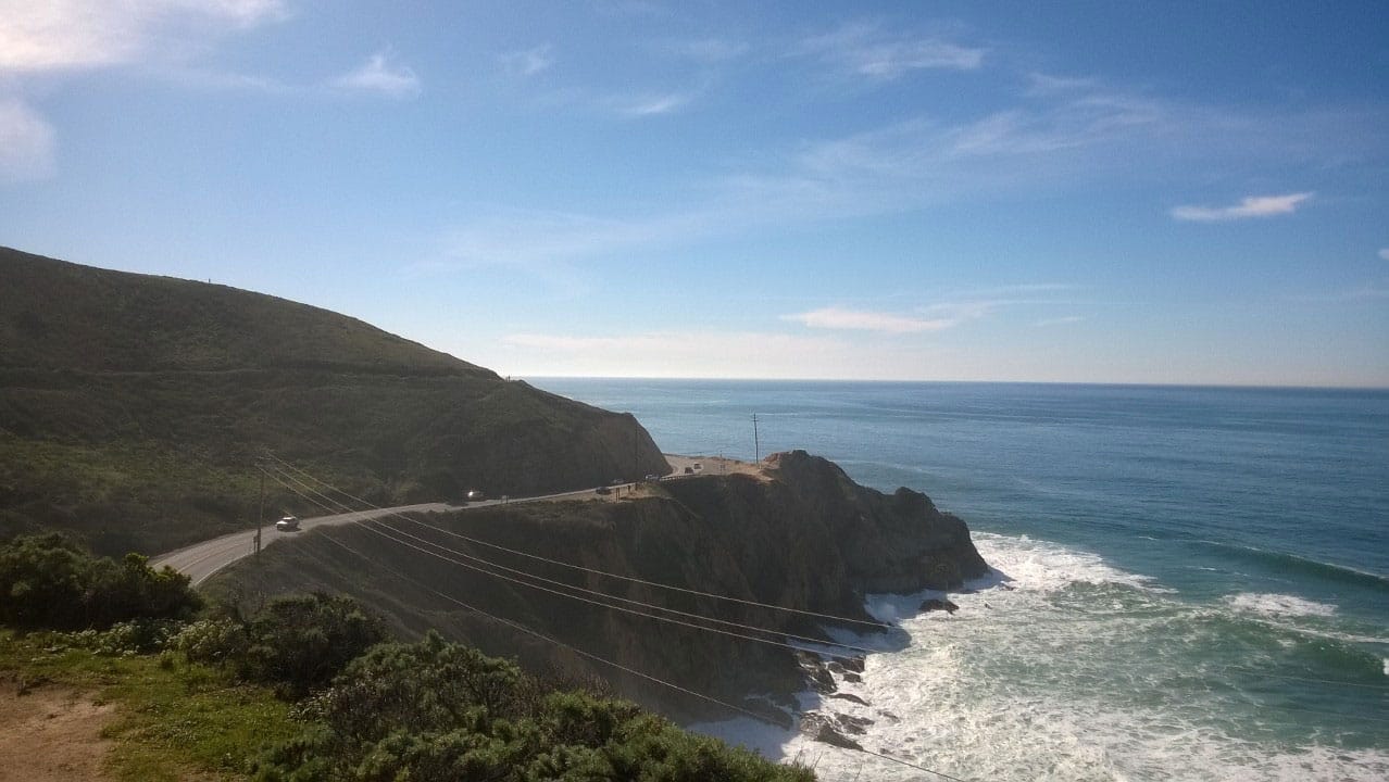 A highway running between a mountainside and a cliff over the ocean.