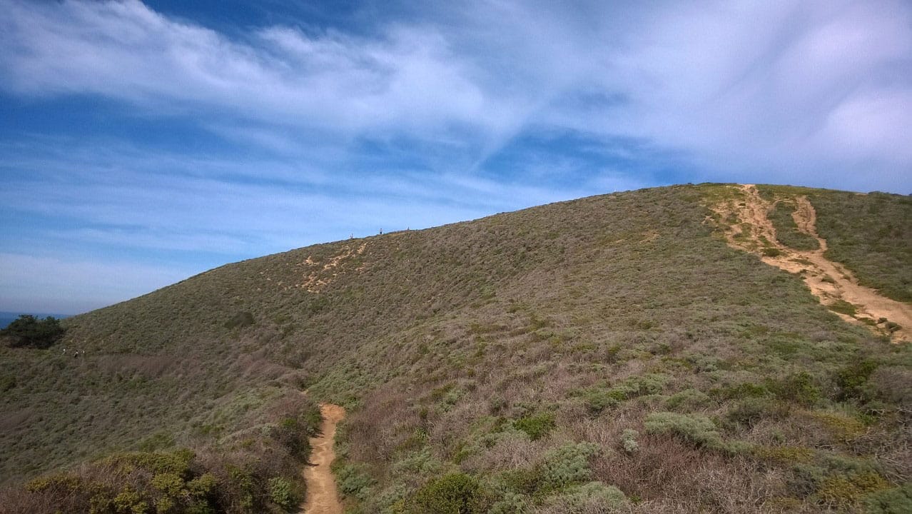 Three distant figures hiking the ridge of a mountain.