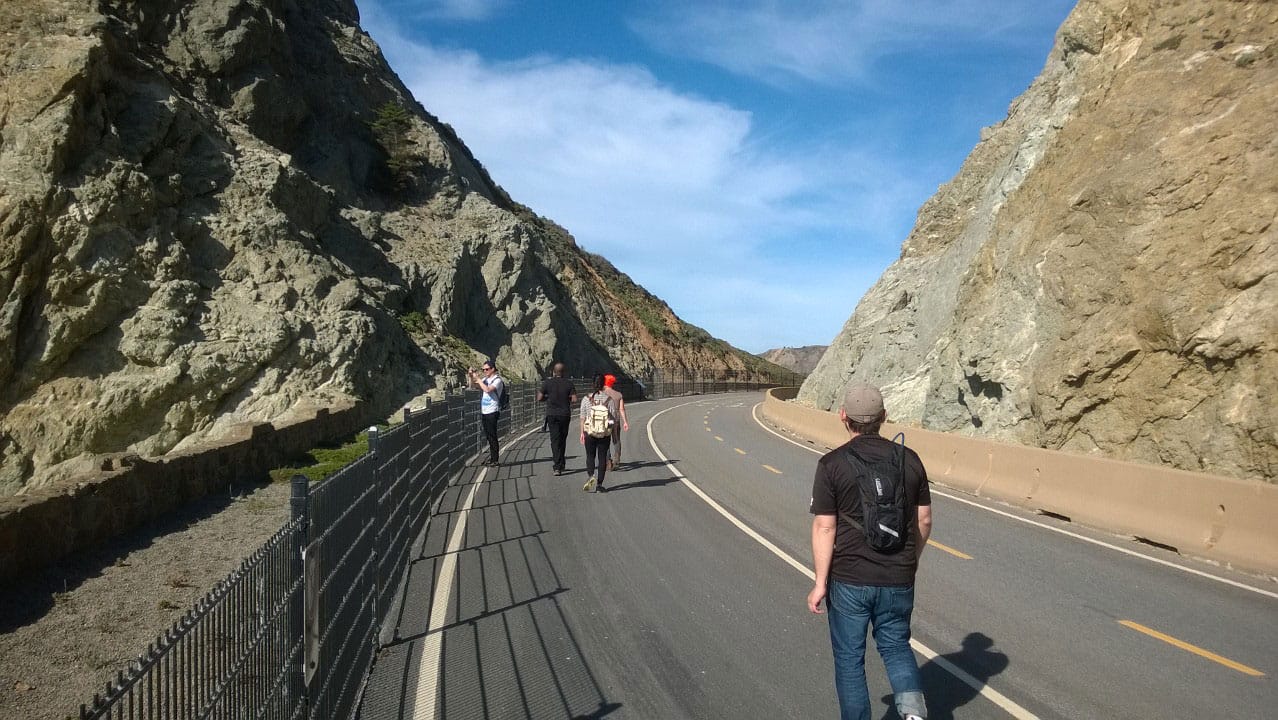 Several people walking along a paved path between two mountains.