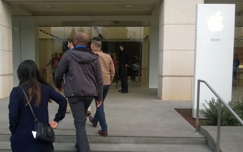 A photograph of several people walking into the front door of an Apple Store